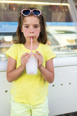 Little girl drinking a lemon iced or slush looking at camera with sunglasses with heart-shapedの写真素材