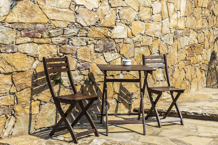 Two chairs and a wooden table on a terrace with stone wallsの写真素材