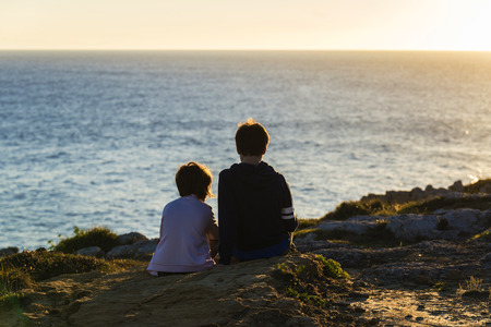 Little girl and teenager boy  looking at the sea on sunsetの写真素材