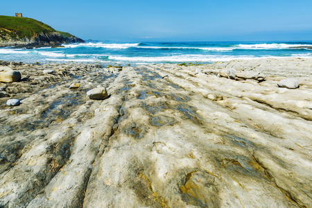 Rocky beach next to cliffs with the tower of San Telmo to the bottom in Ubiarco in Cantabria, Spainの写真素材