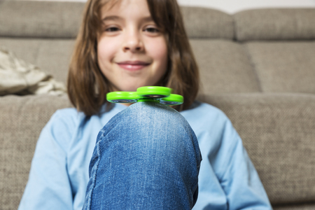 Little girl playing with green fidget spinner toy to relieve stress at homeの写真素材