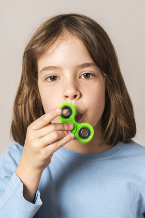 Little girl playing with green fidget spinner toy to relieve stress at homeの写真素材