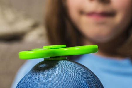 Little girl playing with green fidget spinner toy to relieve stress at homeの写真素材