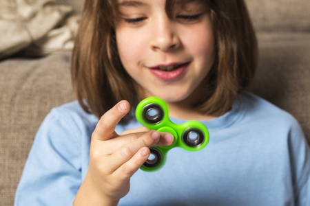 Little girl playing with green fidget spinner toy to relieve stress at homeの写真素材
