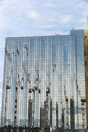 Construction cranes reflected in the glass facade of a skyscraper in Berlin, Germany.の写真素材