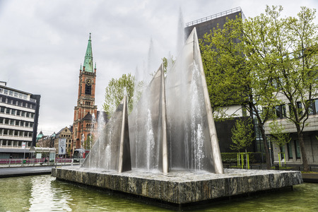 Modern fountain with triangle shape with the church of St John (Johanneskirche) in the background in Dusseldorf, Germanyの写真素材