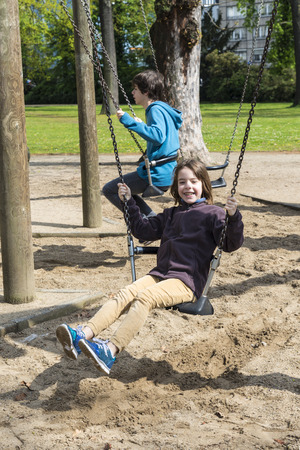 Happy girl and boy laughing and swinging on a swing in a park in autumn in Dusseldorf, Germanyの写真素材