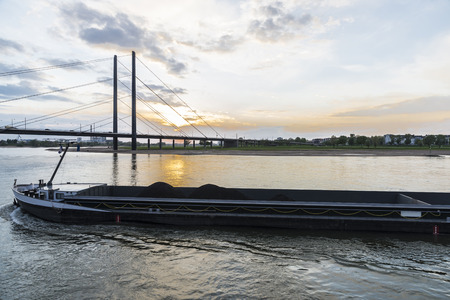 Cargo ship loaded with tons of coal sailing on the Rhine River at dusk in Dusseldorf, Germanyの写真素材