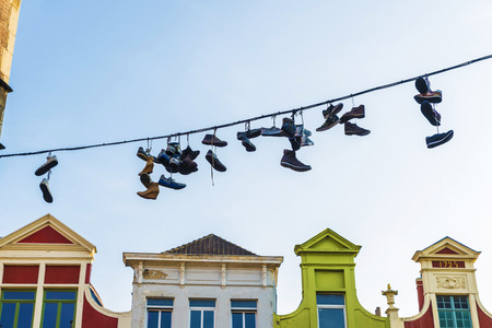 Sneakers and shoes hanging on a cable with the typical old colored houses in the background in the old town of the medieval city of Ghent, Belgiumの写真素材
