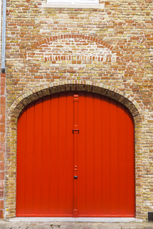 Red door of an old classic building in an old historic center of the medieval city of Bruges, Belgiumの写真素材