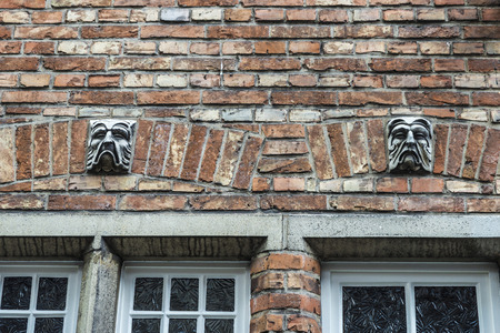 Facade of old historic building with sculptures of angry faces in the medieval city of Bruges, Belgiumの写真素材