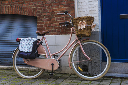 Old vintage bicycle with a wicker basket with ribbons parked on a street in the medieval city of Bruges, Belgiumの写真素材