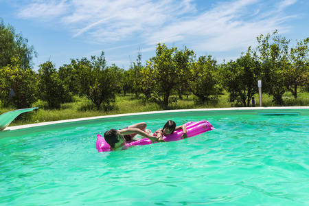 Children playing with a water mat or a float in an outdoor pool between fields of crops in Sicily, Italyの写真素材