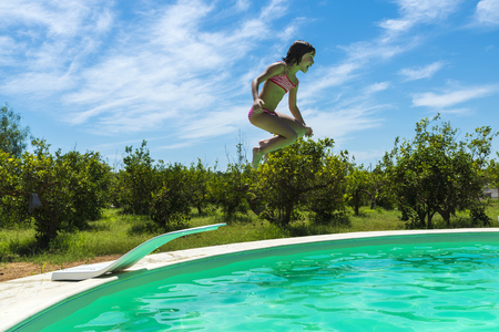 Little girl jumping in pump in an outdoor pool between fields of crops in Sicily, Italyの写真素材