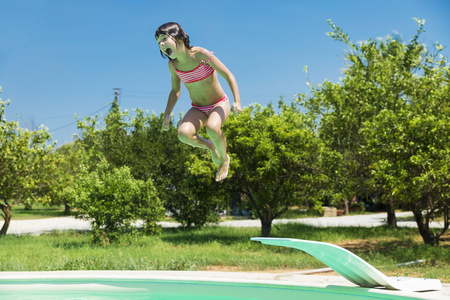 Little girl jumping in pump in an outdoor pool between fields of crops in Sicily, Italyの写真素材