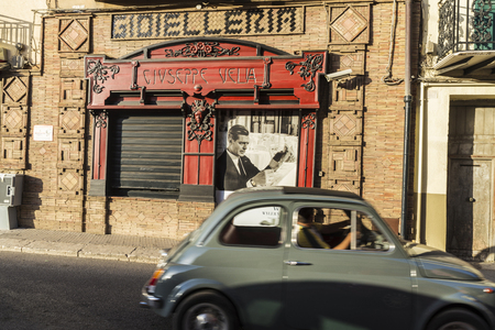 Corleone, Italy - August 9, 2017: Street of the old town of Corleone with a closed jewelry with an old announcement by the Italian actor Marcello Mastroianni while a Fiat 500 passes. Corleone is a town known for associating with the mafia in Sicily, Italyのeditorial素材