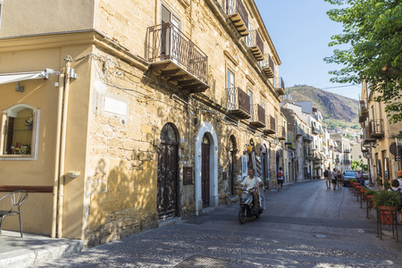 Cefalu, Italy - August 8, 2017: Street with a man carrying a ladder on a motorbike in the old town of the historic village of Cefalu in Sicily, Italyのeditorial素材