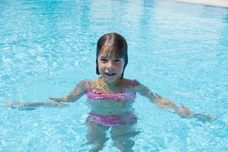 Smiling little girl looking at camera in an outdoor pool in summerの写真素材