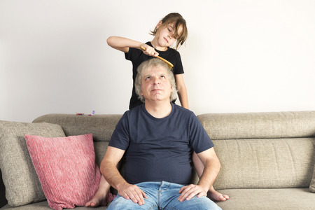 Little girl combing her dad on the couch at homeの写真素材