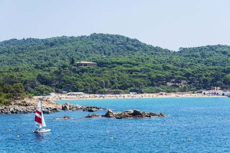Girona, Spain - July 10, 2017: View of Castell beach with a sailboat sailing in Costa Brava, Girona,...