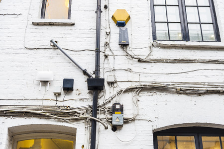 Heap of power cables, communications and alarm on an old white brick wall in London, England, United Kingdomの写真素材