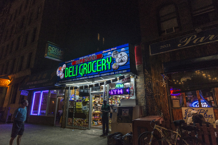 New York City, USA - July 29, 2018: Black man leaving of a grocery at night next to a terrace of a bar with people having a drink on summer in Harlem, Manhattan, New York City, USAのeditorial素材