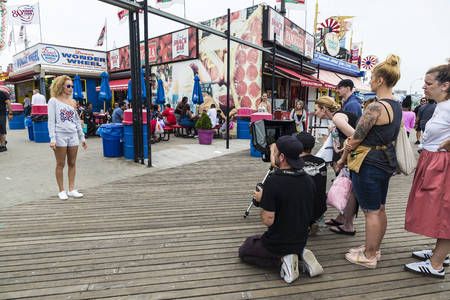 New York City, USA - July 30, 2018: Photographer photographs a fashion model girl at the entrance of the Luna Park amusement park on summer with people around in Coney Island Beach, Brooklyn, New York City, USAのeditorial素材