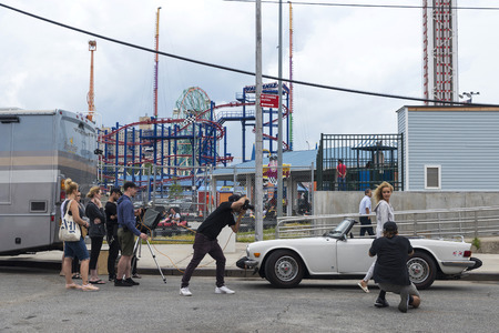New York City, USA - July 30, 2018: Photographer photographs a fashion model girl next to a Triumph TR6, classic convertible sports car, in the Luna Park amusement park on summer with people around in Coney Island Beach, Brooklyn, New York City, USAのeditorial素材
