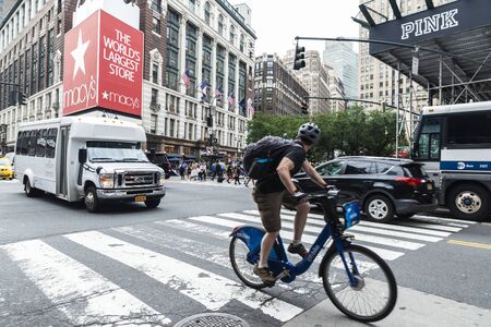 New York City, USA - July 31, 2018: Cyclists and cars on a street with people around in front of...