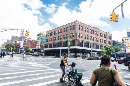New York City, USA - August 1, 2018: Young woman pushing a wheelchair with an old black man on a...