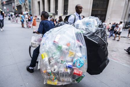 New York City, USA - August 1, 2018: Poor man picking up plastic containers to sell them on a Wall Street in Lower Manhattan, New York City, USAのeditorial素材