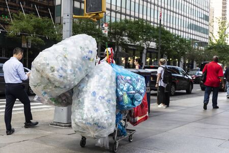 New York City, USA - August 2, 2018: Poor man picking up plastic containers to sell them walking on...