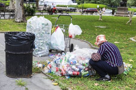 New York City, USA - August 2, 2018: Poor woman picking up plastic containers to sell them on a street with people around in Manhattan, New York City, USAのeditorial素材