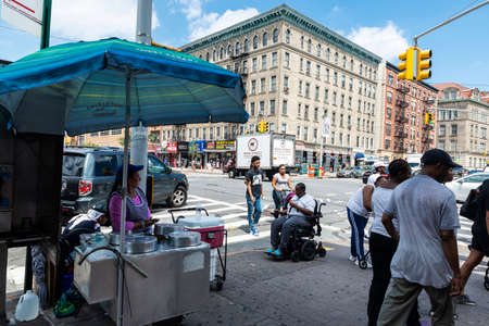New York City, USA - August 3, 2018: Street food stall with its vendor and people around on a street...