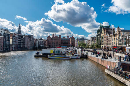 Amsterdam, Netherlands - September 7, 2018: Old traditional leaning houses and tour boats along a canal with people around in Damrak Waterfront, Amsterdam, Netherlandsのeditorial素材