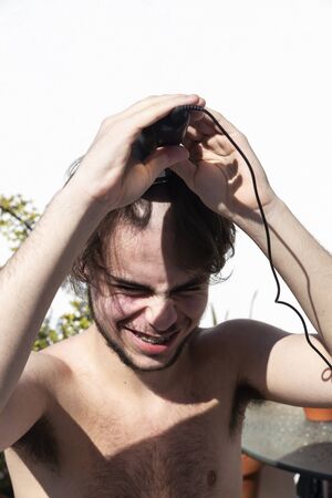 Teen boy cutting his hair with a hair clipper on the balcony of his home during the coronavirus quarantine in Barcelona, Catalonia, Spainの写真素材