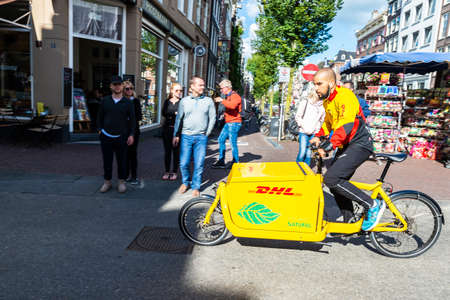 Amsterdam, Netherlands - September 7, 2018: Young man on delivery bicycle DHL circulating and people walking in an old historic center of Amsterdam, Netherlandsのeditorial素材