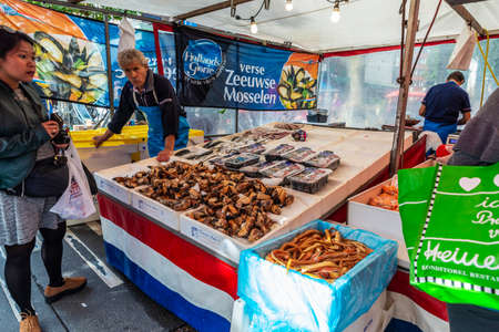 Amsterdam, Netherlands - September 8, 2018: Vendor in a fish and seafood shop with people around in Albert Cuyp Market, street market in Amsterdam, Netherlandsのeditorial素材