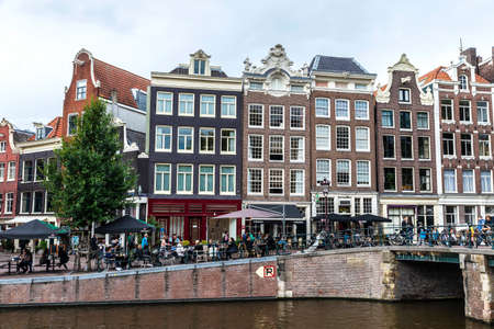 Amsterdam, Netherlands - September 8, 2018: Old traditional leaning houses along a canal with people...