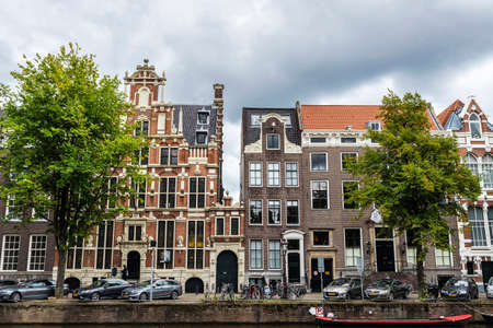 Amsterdam, Netherlands - September 8, 2018: Old traditional leaning houses along a canal with people around in Amsterdam, Netherlandsのeditorial素材