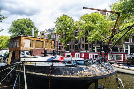 Old rusty ship and a houseboat moored along of a canal in Amsterdam, Netherlandsの写真素材