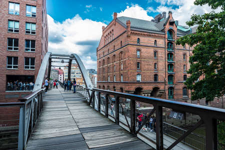 Hamburg, Germany - August 21, 2019: Pedestrian bridge over a canal with people around and an old classic warehouse in HafenCity, Hamburg, Germanyのeditorial素材