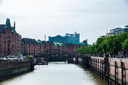 Hamburg, Germany - August 23, 2019: Old warehouses converted into offices and flats next to a canal and the Elbphilharmonie, Elbe Philharmonic Hall, with people around in HafenCity, Hamburg, Germanyのeditorial素材