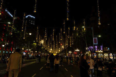 Barcelona, Spain - November 25, 2025: Christmas lights decoration hanging on the street illuminated at night with people around in Passeig de Gracia, Barcelona, Catalonia, Spainのeditorial素材