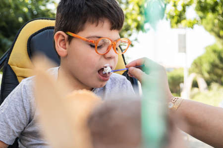 A child in wheelchair eating an ice cream with a spoon.の写真素材