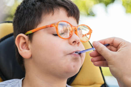 A child in wheelchair eating an ice cream with a spoon.の写真素材