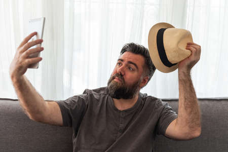 man with beard, hipster, with tablet you take a photo selfie or have a video conference, video call. on the sofa, interior house.の写真素材