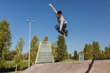 caucasian hispanic roller boy jumps down a ramp from a skate park and does a trick in the air.の写真素材