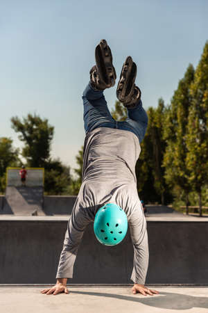 a young male roller skater in a helmet does a dangerous and daring trick on a ramp in a skate park...