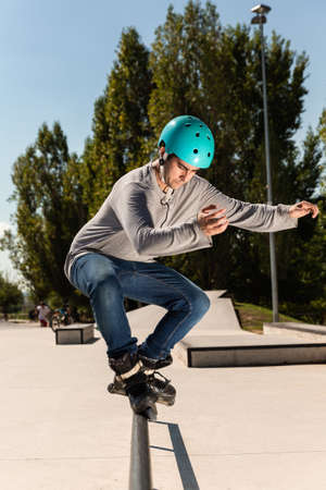 a young male roller skater in a helmet does a dangerous and daring trick on a ramp in a skate park on a sunny day. he wears a t-shirt and jeans.の写真素材